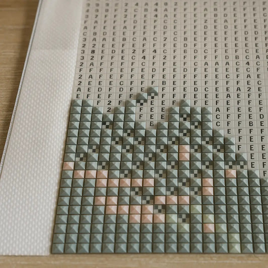 Close-up van gedeeltelijk ingevulde diamond painting met vierkante steentjes in groen, roze en beige op een canvas met letters en cijfers als patroon.