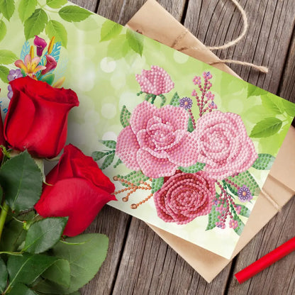 Diamond painting wenskaart met roze rozen en groene bladeren op een houten tafel.