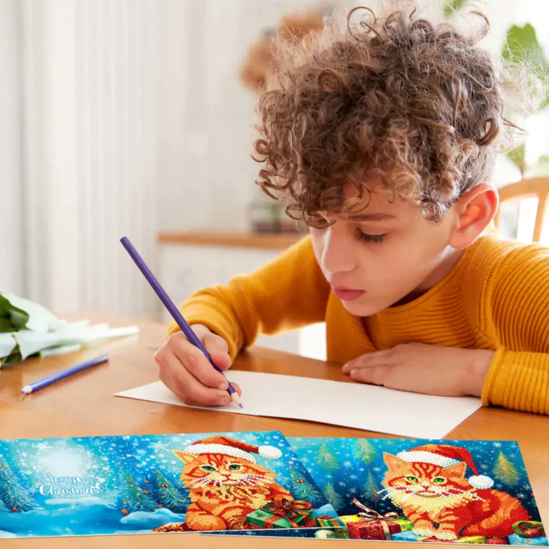 Jonge jongen concentreert zich op het schrijven van een kerstkaart met een afbeelding van een kerstkat in diamond painting stijl op de voorgrond