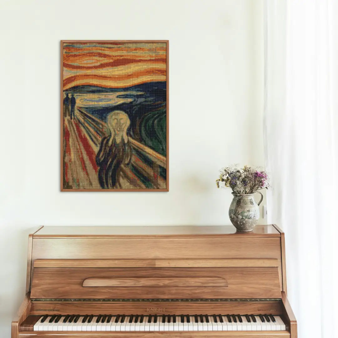 Ingelijst diamond painting van 'De Schreeuw' boven een houten piano met een bloemenvaas.