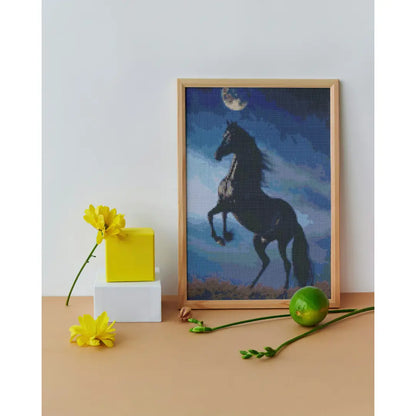 Diamond painting van een steigerend paard onder een volle maan, geplaatst op een oppervlak met gele bloemen en een groene bal.