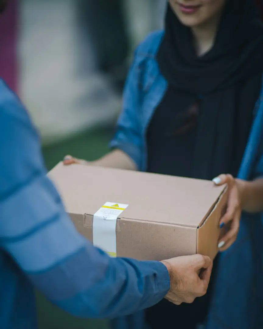 Overdracht van pakket aan vrouw met blauwe sjaal door bezorger in blauw uniform